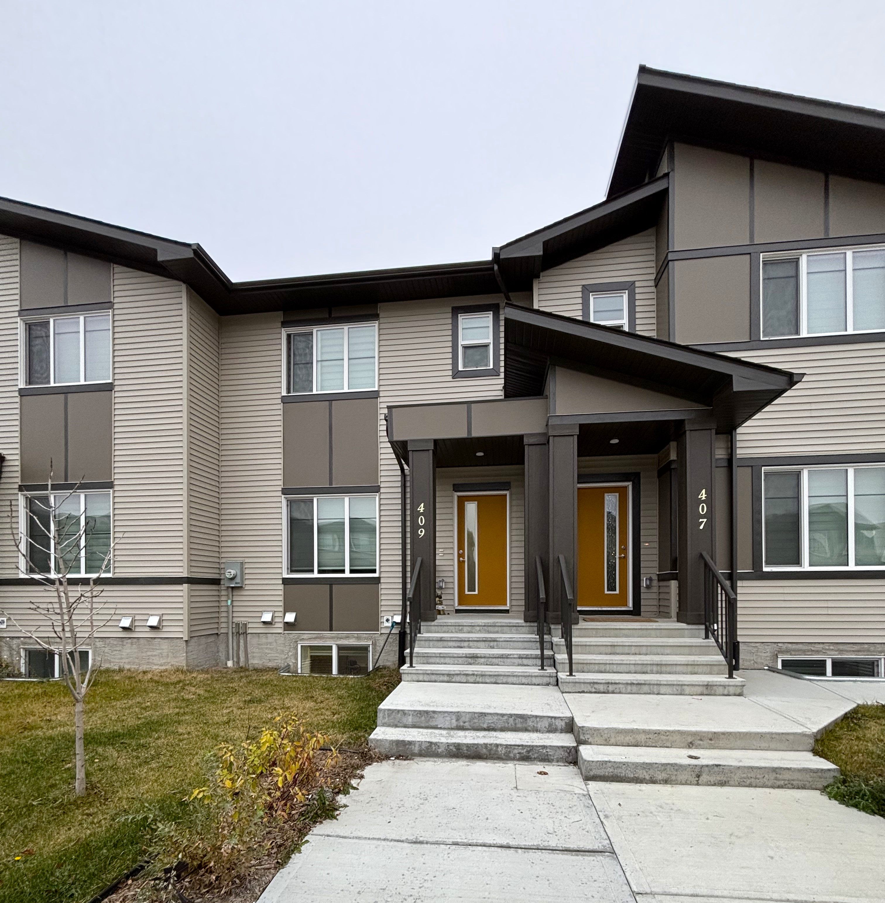 A modern two-story building with a brown and beige exterior and a front door with a brown door and black steps.